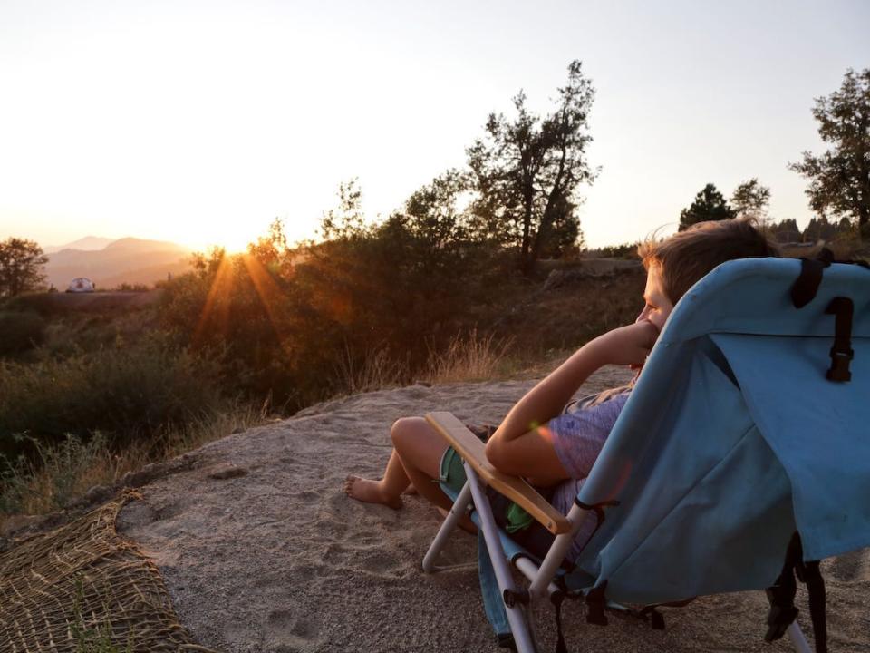 A child sitting on a camping chair watching the sunset.