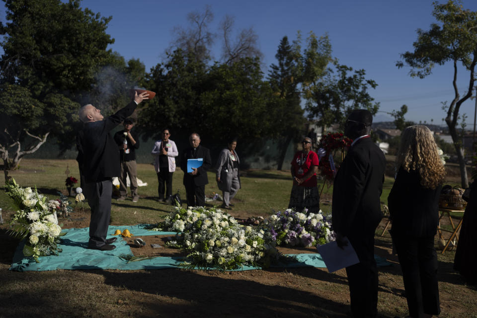 Chaplain Nicholas Jordan, left, holds up a bowl of incense during the Los Angeles County ceremony of the unclaimed dead at a county cemetery in Los Angeles, Thursday, Dec. 14, 2023. This year's service laid to rest 1,937 people who died unclaimed in 2020. They were immigrants, children, people experiencing homelessness or poverty, and, for the first time, victims of the coronavirus. (AP Photo/Jae C. Hong)