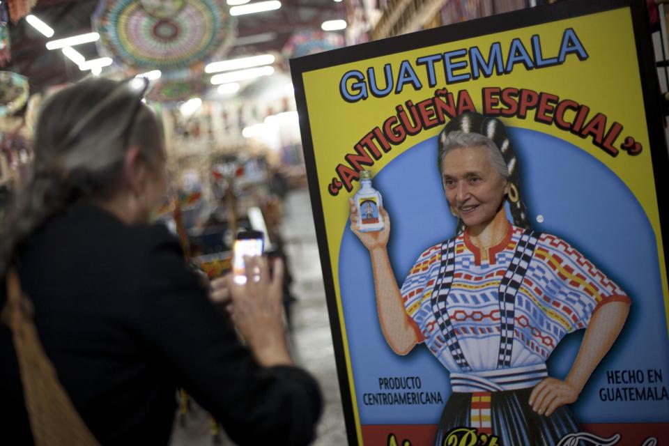 In this Nov. 14, 2013 photo, a tourist pose for her friend behind a cut-out sign advertising a local beverage at the market in Antigua, Guatemala. Antigua attracts tourists from all over the world with its crumbling colonial charm, and an elaborate procession that winds through the city’s streets around Lent. (AP Photo/Luis Soto)