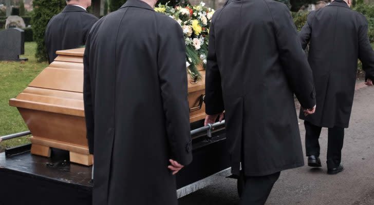 people in suits carry a casket at a funeral