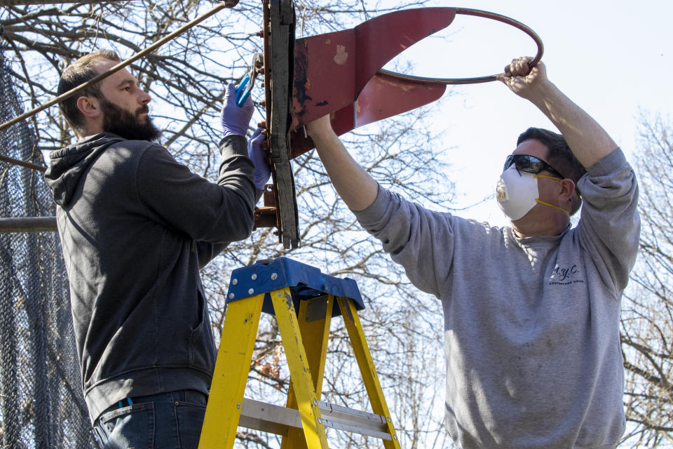 New York City Department of Parks and Recreation employees remove the basketball hoop from a court in Tompkins Square Park, Thursday, March 26, 2020, in New York. Across the U.S., police departments are taking a lead role in enforcing social distancing rules that health officials say are critical to containing the coronavirus. In New York City, they've started dismantling basketball hoops to prevent people from gathering in parks and playing. (AP Photo/Mary Altaffer)