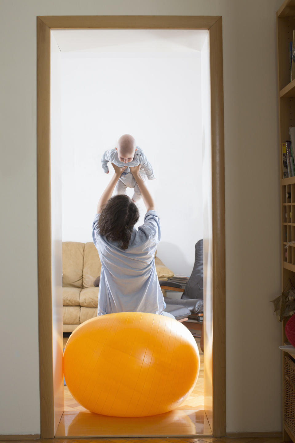 A mom hoisting her child in the air while sitting on a yoga ball