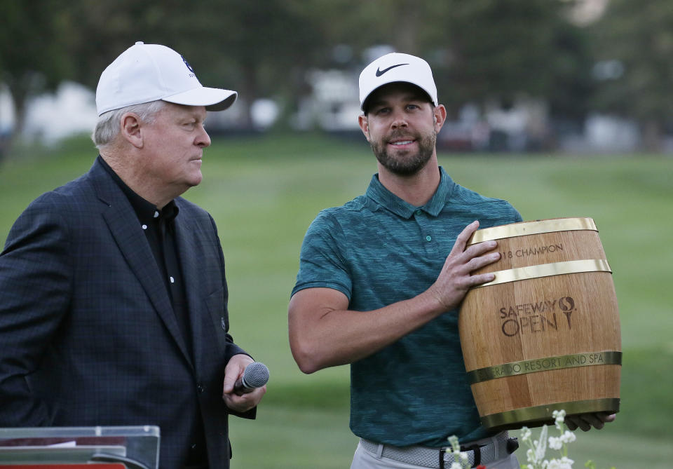 Kevin Tway holds his trophy on the 18th green of the Silverado Resort North Course after winning the Safeway Open PGA golf tournament Sunday, Oct. 7, 2018, in Napa, Calif. Tway won the tournament on the third playoff hole. At left is broadcaster and host Johnny Miller. (AP Photo/Eric Risberg)