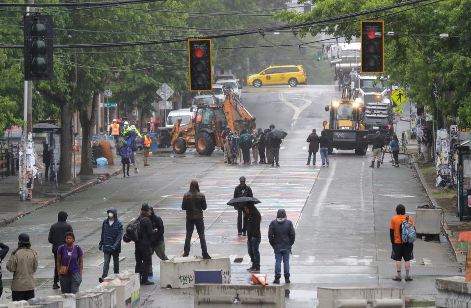 Protesters gather a block away as Seattle Department of Transportation workers remove barricades at the intersection of 10th Avenue and Pine Street June 30 in Seattle.