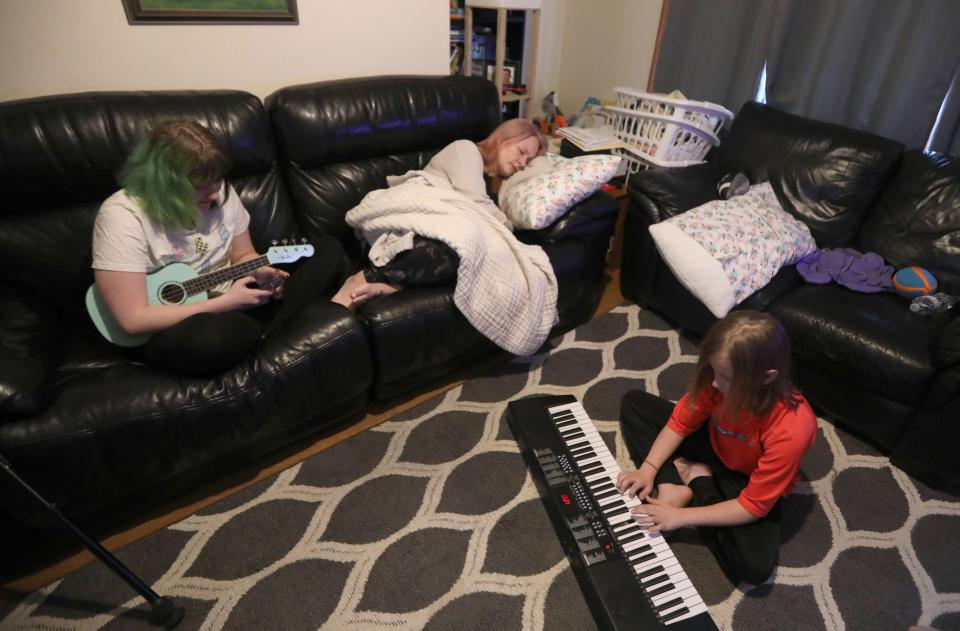 Rebekah Hogan rests in the living room of the family's home in Troy, N.Y. April 7, 2022 while her daughter Caleigh, 15, and son Sebastian, 9, play their musical instruments. The family of five, including Rebekah's husband James, a disabled military veteran and son Ben, 14, contracted COVID-19 in late 2020. Almost a year and a half later, they all suffer symptoms of long COVID. James, who is permanently disabled, has had to take on the role of caregiver for his family despite his lingering symptoms. Rebekah, a registered nurse, has been unable to work due to her COVID symptoms. As a result the family has eaten into much of their life savings. 