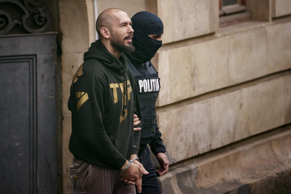 FILE - A police officer escorts Andrew Tate, left, from the Court of Appeal in Bucharest, Romania, Tuesday, March 12, 2024. A court in Romania's capital on Friday, April 26, 2024, ruled that a trial can start in the case of influencer Andrew Tate, who is charged with human trafficking, rape and forming a criminal gang to sexually exploit women.(AP Photo/Andreea Alexandru, File)