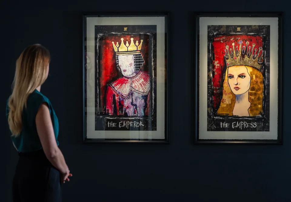 A woman looking at two paintings hanging on a dark background