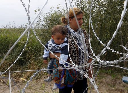 A Syrian migrant carries a child while standing behind a fence before crossing the Hungarian-Serbian border near Asotthalom, Hungary August 25, 2015. REUTERS/Laszlo Balogh