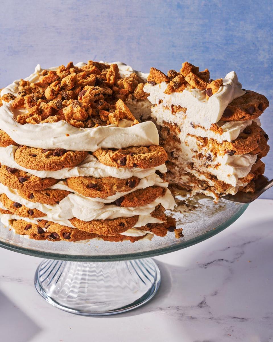 icebox cake made of chocolate chip cookies and whipped cream layered on a cake stand in front of a blue background