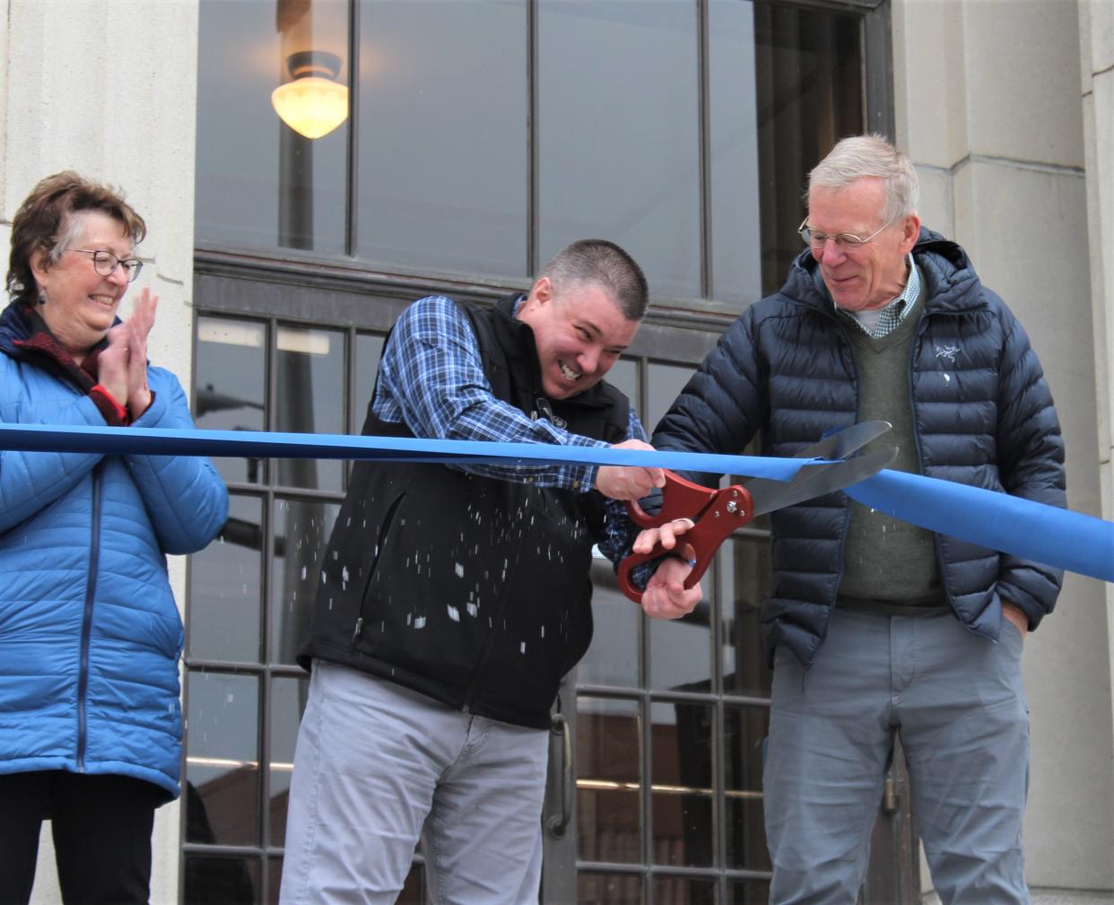 Great Falls Mayor Cory Reeves struggles to cut the blue ribbon officially dedicating the revitalization project of the Great Falls Civic Center, as former mayor Brian Kelly (right) and city commissioner Susan Wolff cheer him on