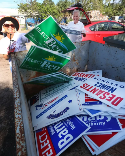 Suze Peace and Peter Sigmann toss election yard signs into a dumpster for recycling in 2018. Peace's efforts are continuing in 2022 to divert the plastic signs from landfills.