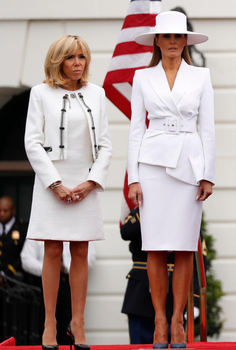 Melania Trump and Brigitte Macron in white outfits standing in front of the White House