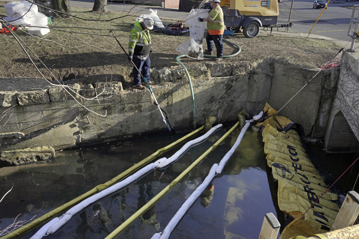 Two workers in yellow jackets place yellow and white booms in a body of water faced with concrete.