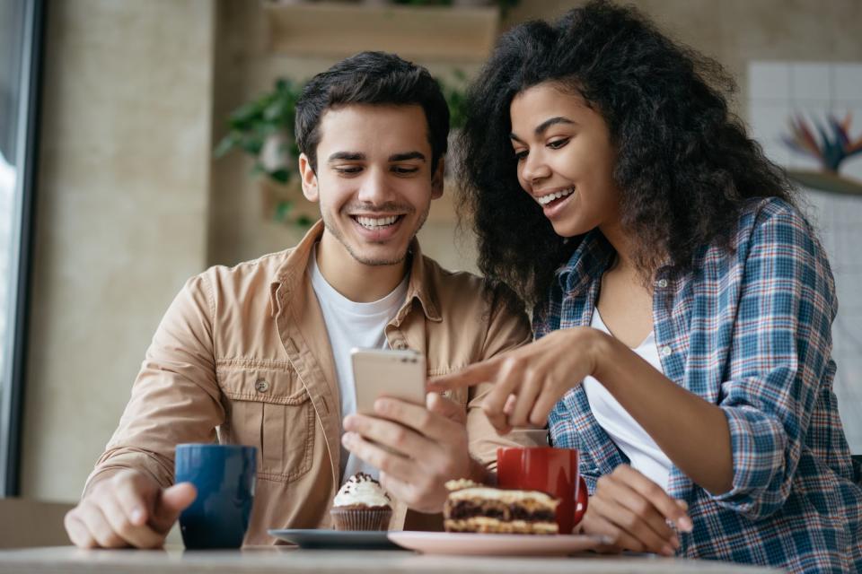 Two investors smile while looking at something on a phone in a kitchen.