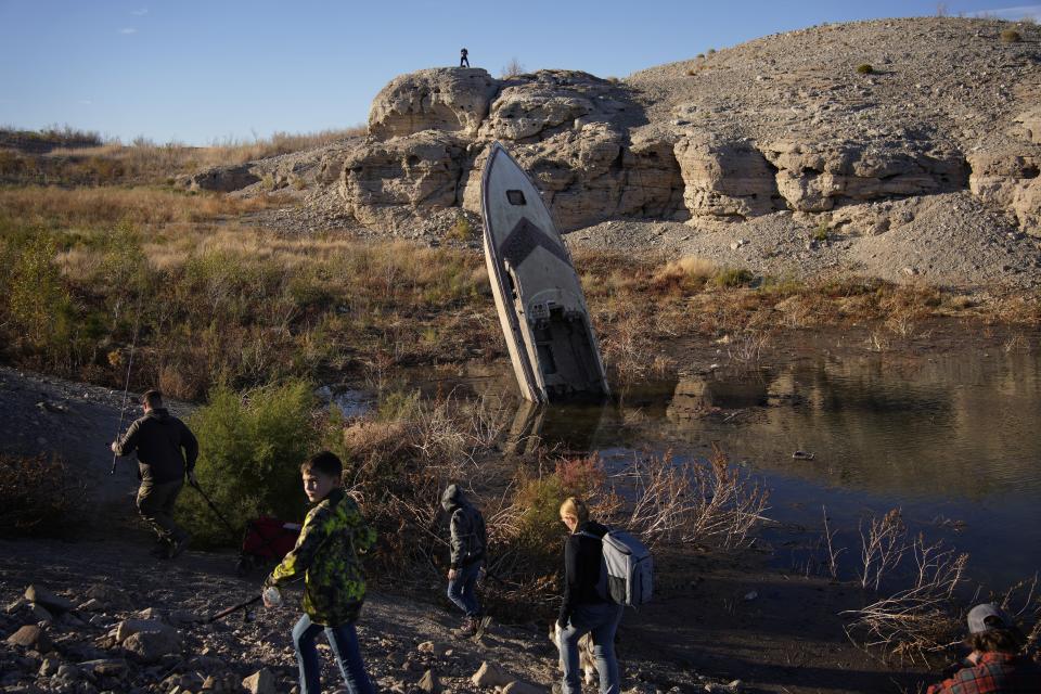 FILE - People walk by a formerly sunken boat standing upright into the air with its stern buried in the mud along the shoreline of Lake Mead at the Lake Mead National Recreation Area, Jan. 27, 2023, near Boulder City, Nev. (AP Photo/John Locher, File)