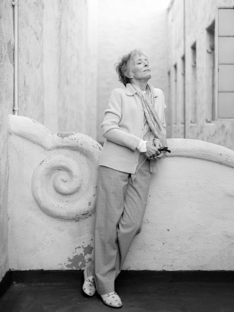 A black-and-white portrait of a standing woman leaning against an ornate wall.