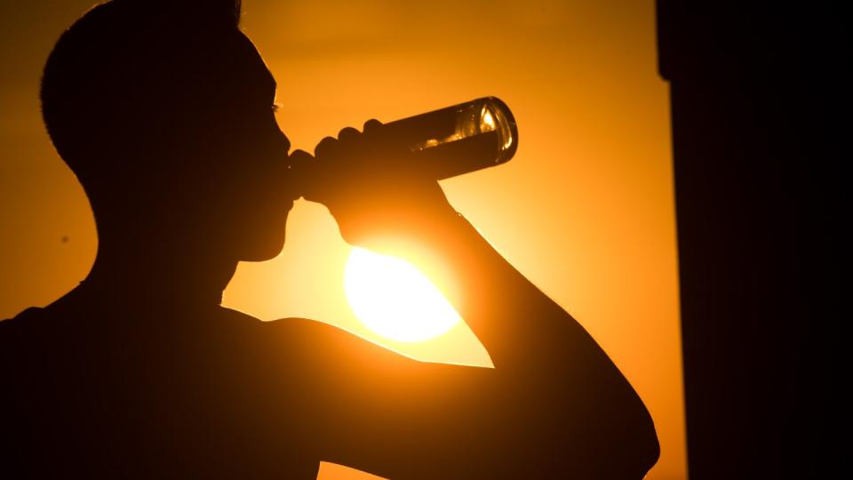 Ein junger Mann sitzt auf dem Kronsberg und trinkt Bier, während am Horizont die Sonne untergeht.