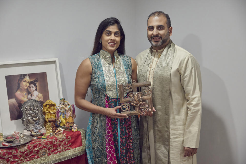 Sheetal Deo and her husband, Sanmeet Deo, hold a Hindu swastika symbol in their home in Syosset, N.Y., on Sunday, Nov. 13, 2022. Hindus, Buddhists and Native Americans are trying to rehabilitate the swastika, a symbol of peace and prosperity, and to restore it to a place of sanctity in their faiths. (AP Photo/Andres Kudacki)