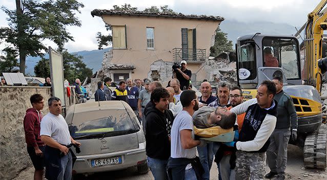 A man is carried out on a stretcher as a collapsed building is seen in the background. Photo: AP/Alessandra Tarantino