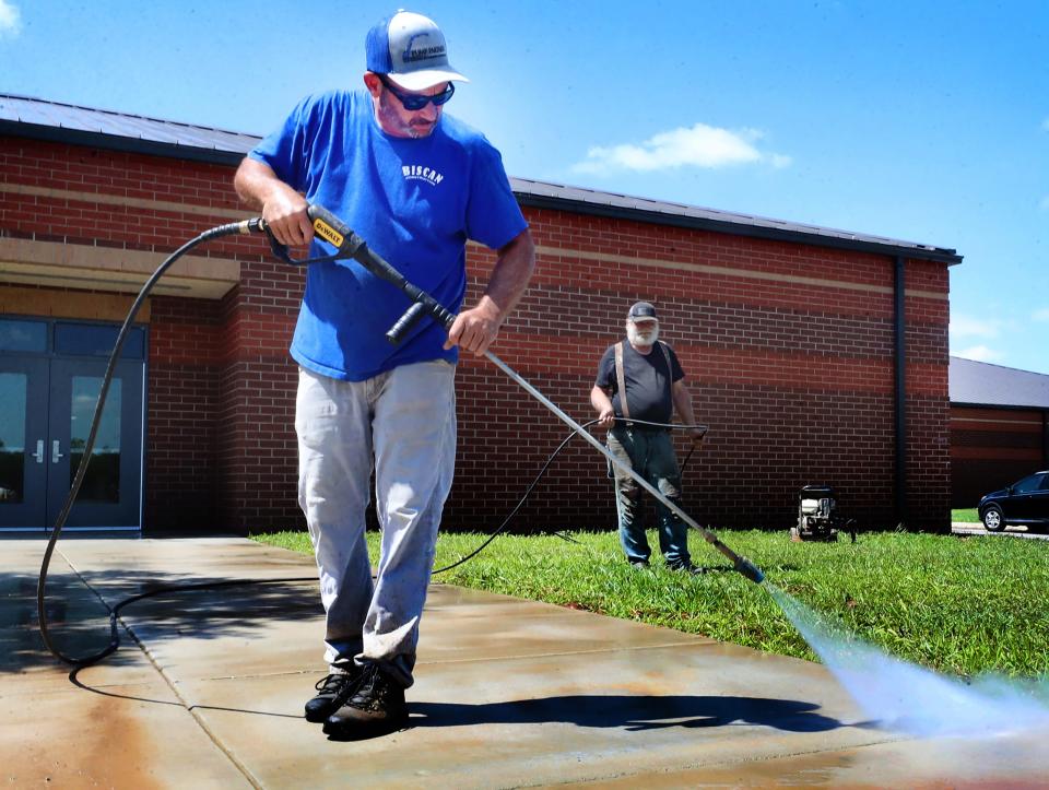 Bob Elder with Robert Biscan Construction, pressure washes the sidewalk at Rockvale Middle school as his co-worker Robert Shrum holds the hose in the background as they cleanup after completing an addition to the middle school on Tuesday, July, 11, 2023. 