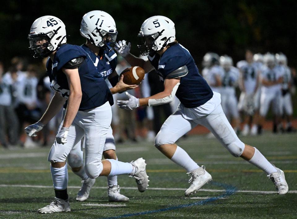 Medway quarterback Luke Frauton (11) hands off to Henry Comras before Comras carried for a touchdown during the first half against Westwood at Medway High School, Sept. 29, 2022.