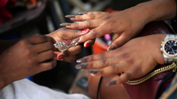 A manicurist applies nail polish to a customer's nails outside a street salon in the Ikeja district of Lagos, Nigeria, 01 June 2022.