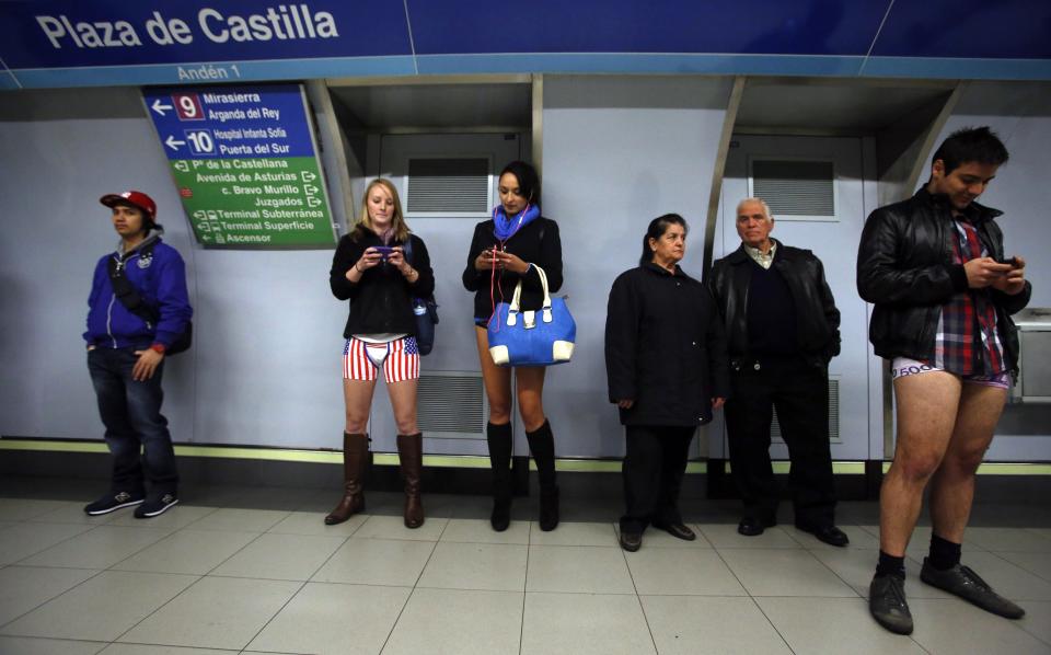 Passengers without their pants check their mobile phones as they wait for a train during the "No Pants Subway Ride" event in Madrid