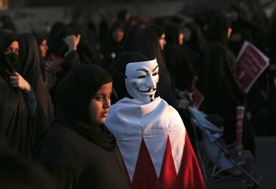 Bahraini pro-democracy protesters, one wearing a Guy Fawkes mask on the back of her head and a national flag, participate in a march near Saar, west of the capital of Manama, Bahrain, Saturday, Feb. 15, 2014. Tens of thousands of protesters marched down a divided four-lane highway, calling for the long-serving prime minister, Sheik Khalifa bin Salman Al Khalifa, to step down and for democracy in the Gulf island kingdom. (AP Photo/Hasan Jamali)