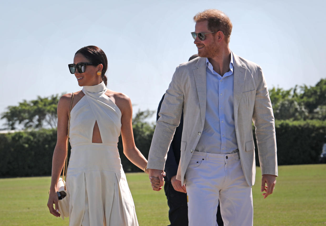 Harry and Meghan wearing sunglasses and holding hands in the sunshine on a polo field in Florida