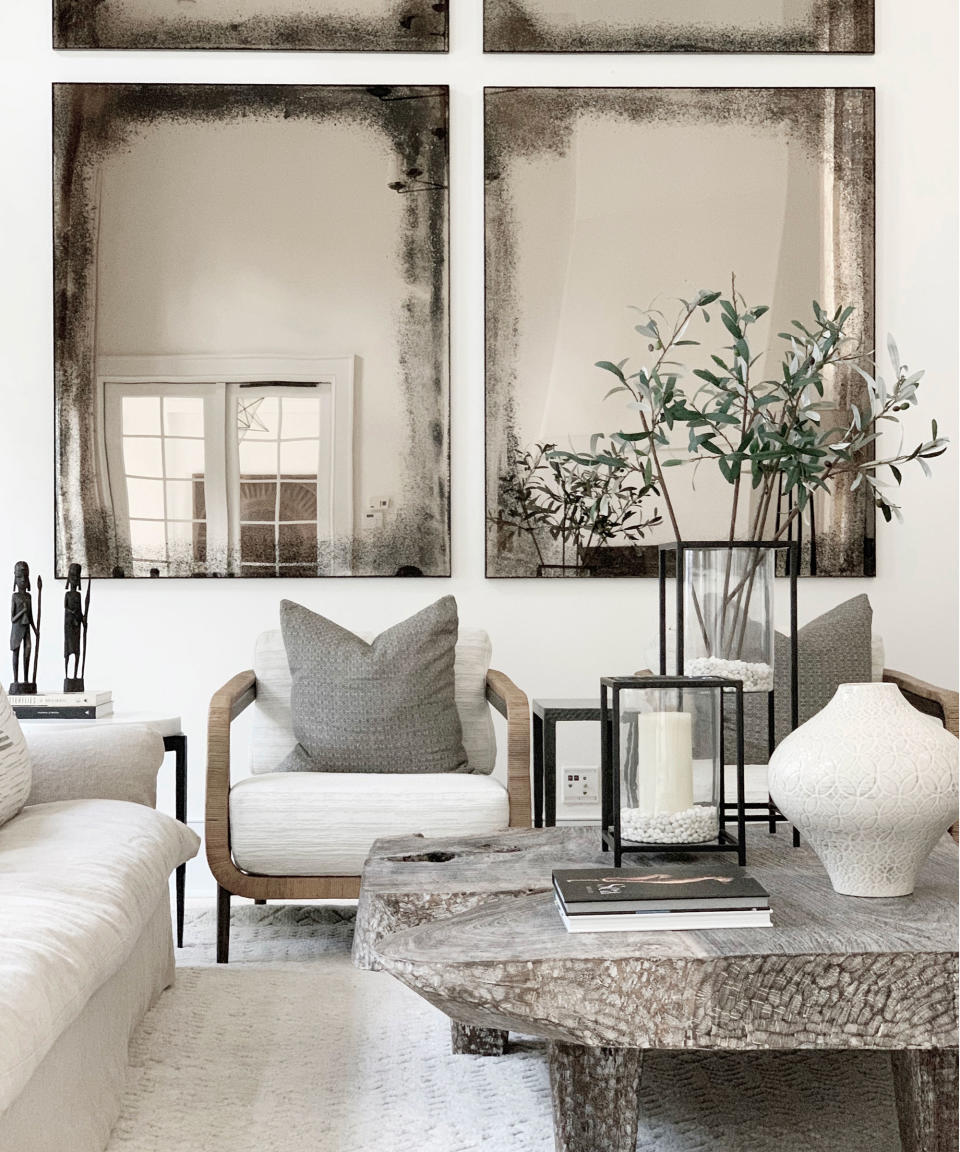 Wall of acid wash mirrors behind white and wooden armchairs in modern living room with stone coffee table