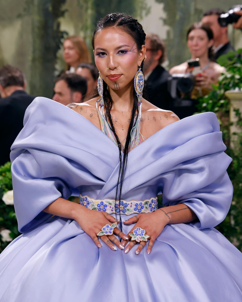 Quannah Chasinghorse in a large puffy-sleeved dress with floral accents, sporting long earrings and braided hair