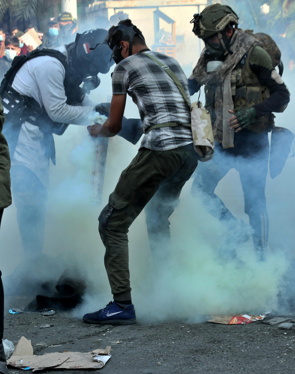 Anti-government protesters take a tear gas canister fired by security forces and extinguish it in a container during clashes on Rasheed Street in Baghdad, Iraq, Tuesday, Nov. 26, 2019. (AP Photo/Hadi Mizban)