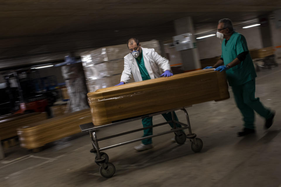 workers move a coffin with the body of a victim of coronavirus as others coffins are stored waiting for burial or cremation at the Collserola morgue in Barcelona, Spain, Thursday, April 2, 2020. The new coronavirus causes mild or moderate symptoms for most people, but for some, especially older adults and people with existing health problems, it can cause more severe illness or death. (AP Photo/Emilio Morenatti)