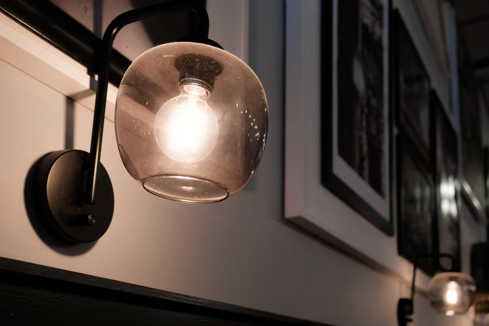 A close-up of a modern wall light fixture with an exposed bulb, mounted on a wall adorned with framed pictures