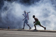 Indigenous clashing with police walk through clouds of tear gas outside Congress in Brasilia, Brazil, Tuesday, June 22, 2021. Indigenous who are camping in the capital to oppose a proposed bill they say would limit recognition of reservation lands clash with police who blocked them from entering Congress. (AP Photo/Eraldo Peres)