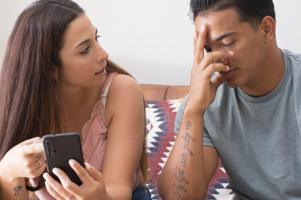 a woman holding a phone and looking at her significant other with an upset face