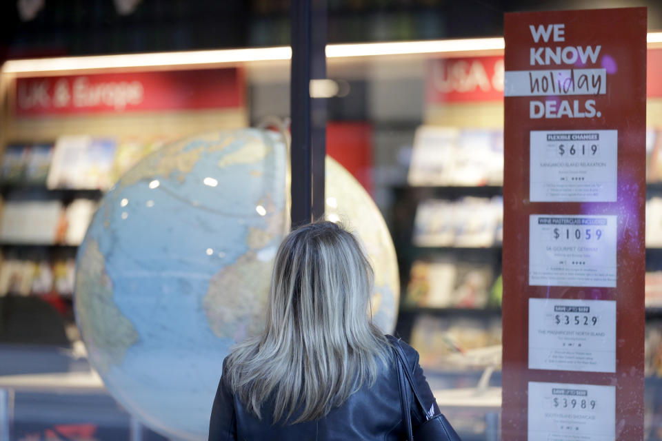 A woman looks at ads in the window of a closed travel agent office in Sydney, on Aug. 13, 2021. Japan, Australia and New Zealand all got through the first year of the coronavirus pandemic in relatively good shape, but now are taking very divergent paths in dealing with new outbreaks of the fast-spreading delta variant. (AP Photo/Rick Rycroft)