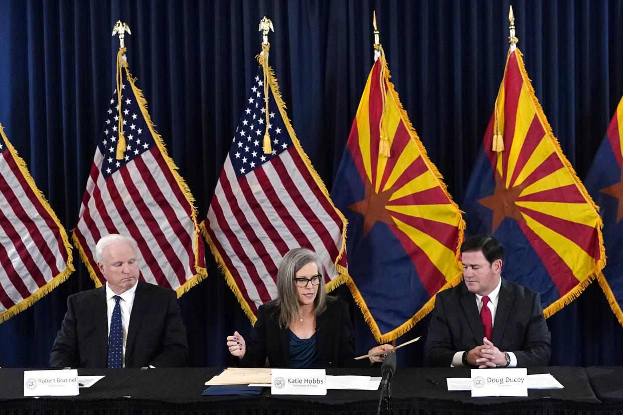 Arizona Democrat governor-elect and current Arizona Secretary or State Katie Hobbs, middle, passes to Arizona Republican Gov. Doug Ducey, right, official certification documents to sign for the Arizona general election canvass in a ceremony as Arizona Supreme Court Chief Justice Robert Brutinel, left, looks on at the Arizona Capitol in Phoenix, Monday, Dec. 5, 2022. (AP Photo/Ross D. Franklin, Pool)