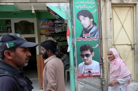 A policeman (L) and residents walk past a shop displaying the pictures of men, who were killed in a suicide blast on January 2015, in a Shi'ite mosque in Shikarpur, Pakistan March 19, 2017. Picture taken March 19, 2017. REUTERS/Akhtar Soomro