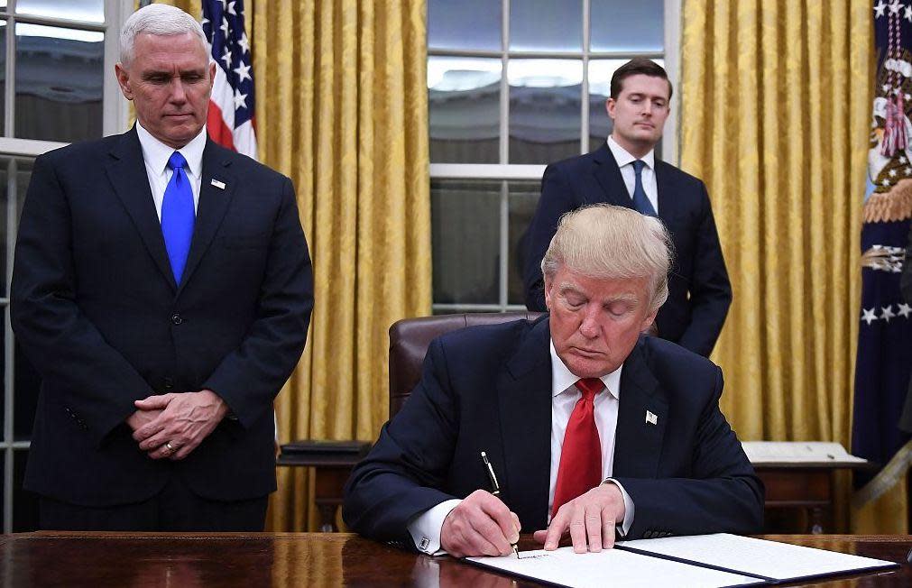 President Donald Trump signs an executive order as Vice President Mike Pence looks on at the White House in Washington, DC on January 20, 2017: Jim Watson/Getty