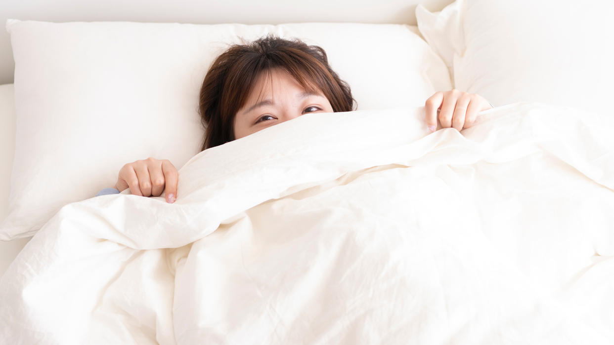  How to clean a duvet: woman in bed poking her head out from under the duvet. 