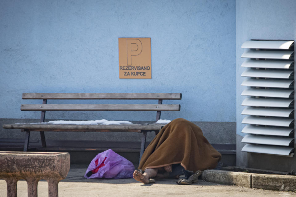 A migrant sits on the pavement to warm up outside the Miral camp, in Velika Kladusa, Bosnia, Wednesday, April 7, 2021. Bosnia is seeing a rise in coronavirus infections among migrants and refugees living in its camps, as it struggles to cope with one of the Balkans' highest COVID-19 death and infection rates among the general population.(AP Photo/Davor Midzic)