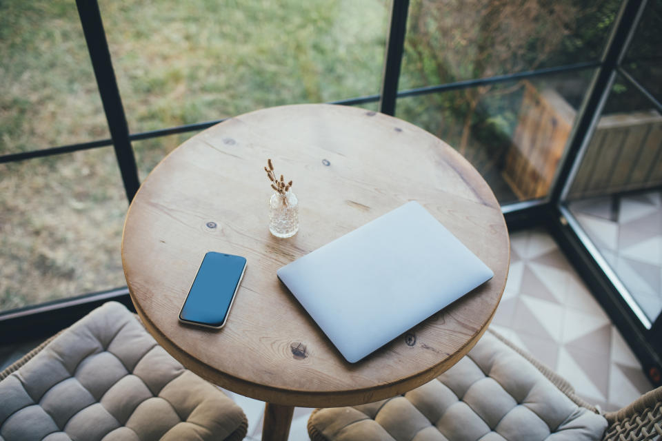 Laptop and smartphone on a round wooden table in a cozy interior.