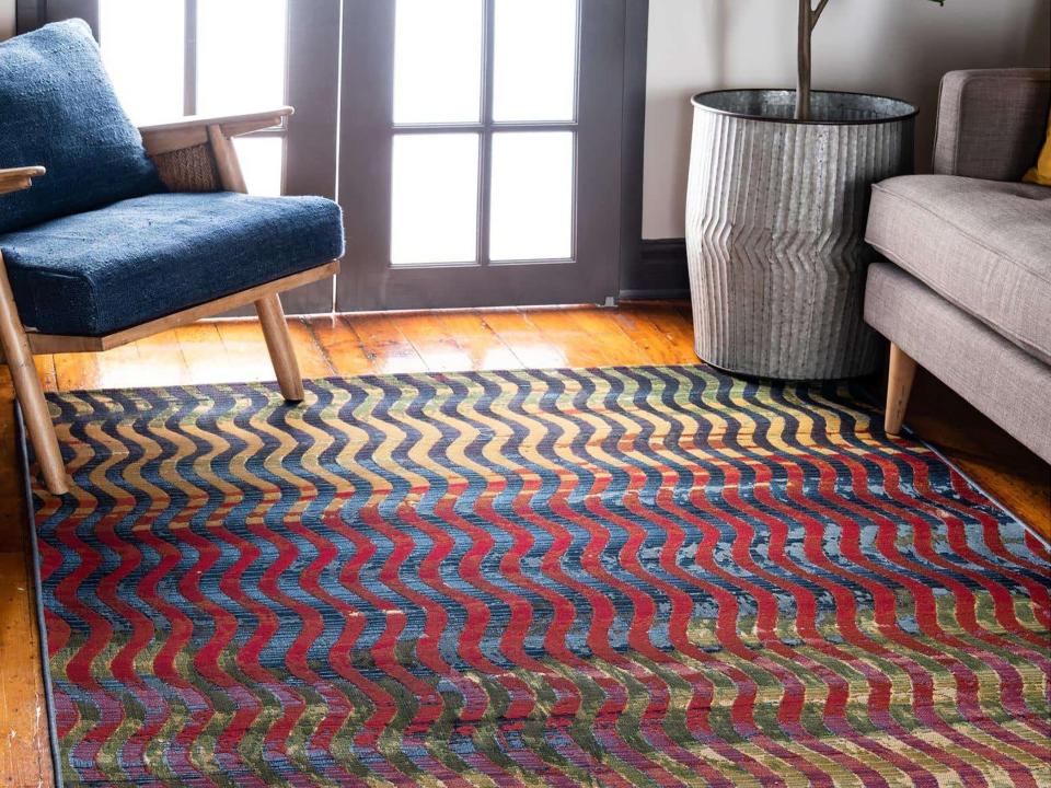 A multicolored rug with a blue chair and a gray couch and plant in corner