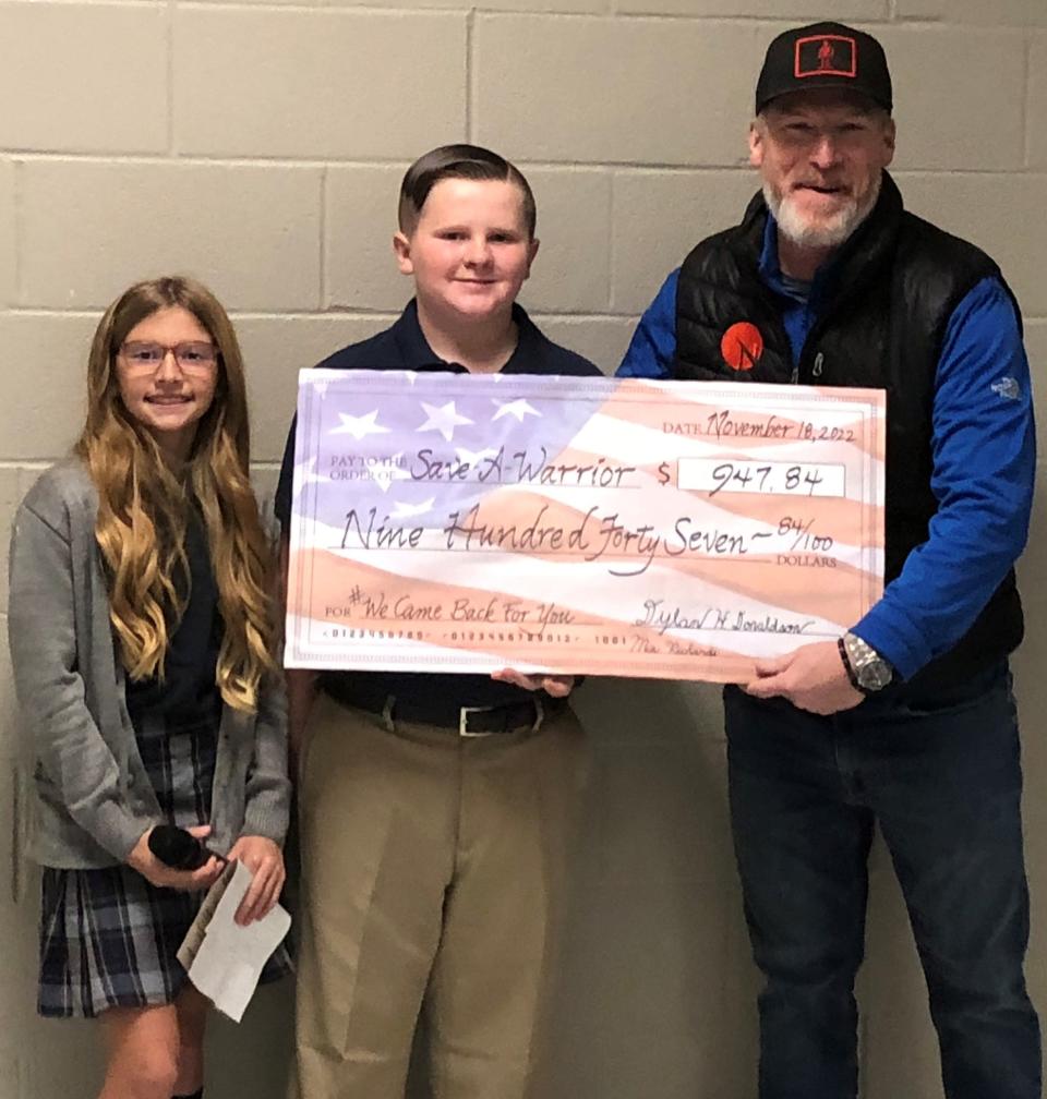 Jake Clark, founder of Save A Warrior, receives a check for $947.84 from Blessed Sacrament fifth graders Mia Richards and Dylan Donaldson. They raised the money through the school's Romans 12 program.