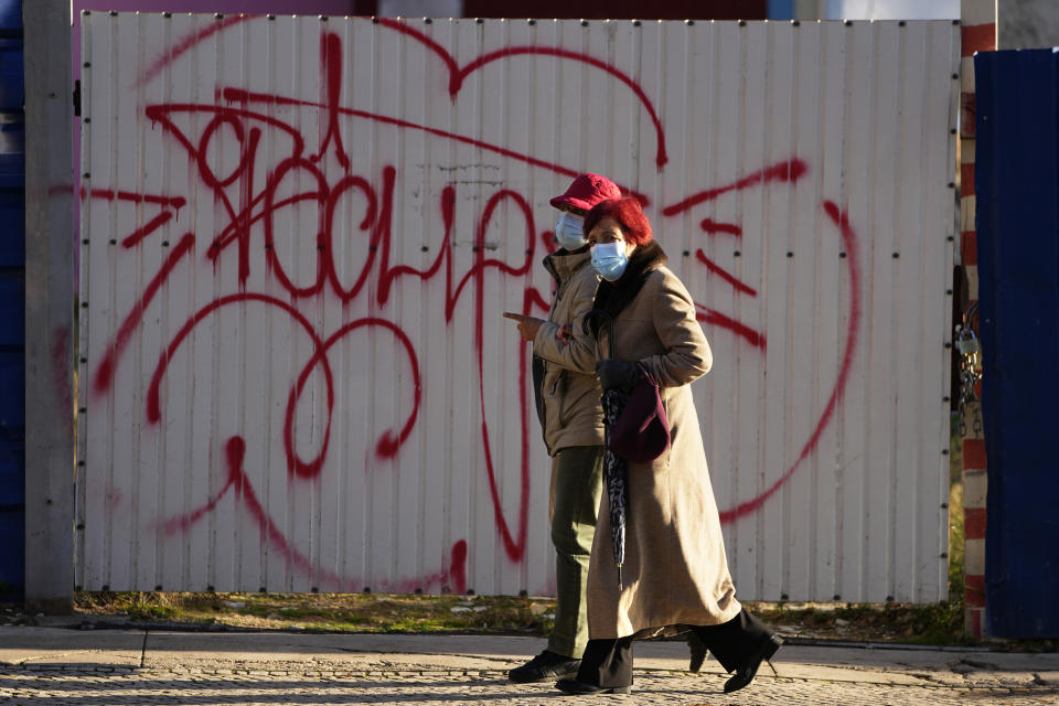 Two women wearing face masks walk along a street in Lisbon, Thursday, Nov. 25, 2021. Portugal is reporting its highest number of new daily COVID-19 infections since July amid a surge in cases across Europe. The Portuguese government is due to announce on Thursday what new pandemic restrictions it is introducing, seven weeks after scrapping almost all of them due to the high vaccination rate. (AP Photo/Armando Franca)