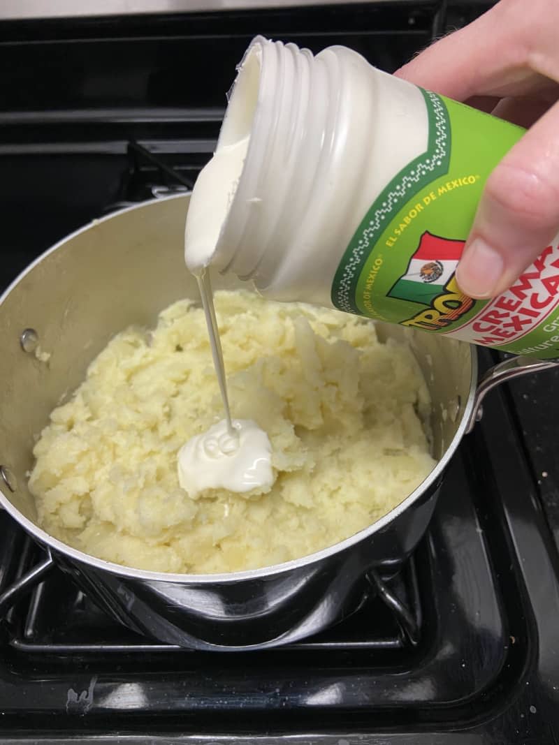 Cream is being poured into a plan of potatoes.