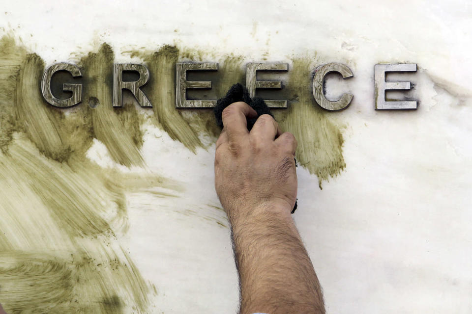 A worker cleans graffiti off the Bank of Greece logo, outside the central bank's headquarters in Athens.