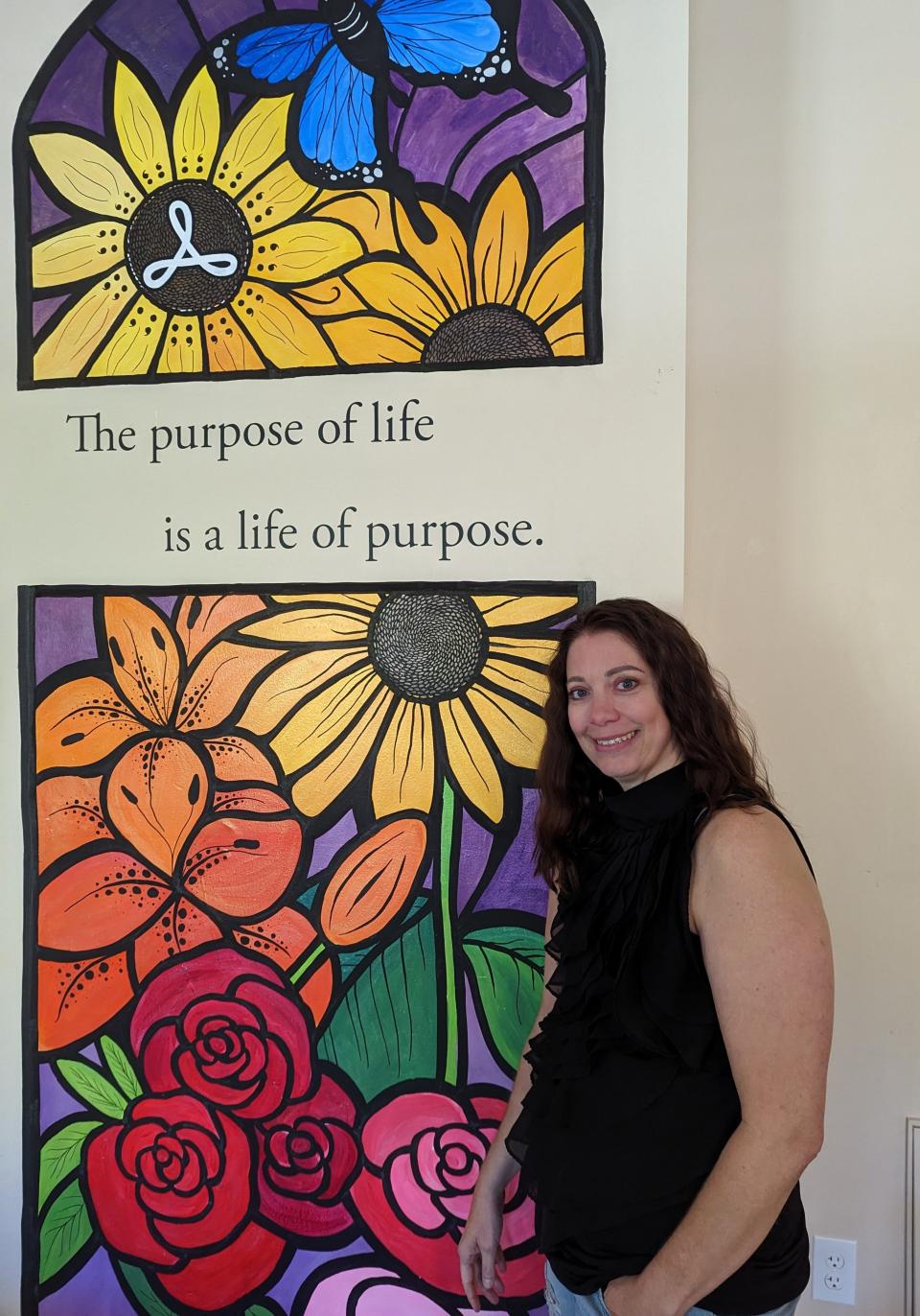Shannon Ortiz stands in front of a sunflower mural created by her friend, artist Sarah Wohlgamuth, at the Hope & Healing Center in Canton. The sunflower, a  symbol of loyalty and happiness, also features semi-colons in support of Project Semicolon, a mental-heath advocacy group.