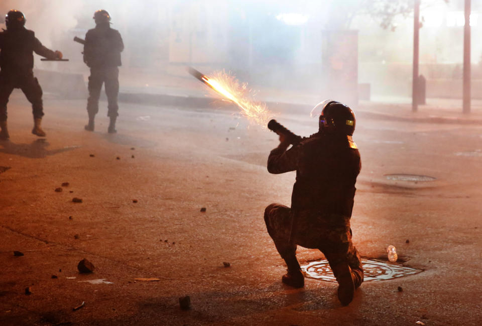 A riot policeman fires tear gas against the anti-government protesters, during ongoing protests against the Lebanese central bank's governor and against the deepening financial crisis, at Hamra trade street, in Beirut, Lebanon, Tuesday, Jan. 14, 2020. Lebanese security forces lobbed tear gas at protesters who responded with rocks outside the country's central bank Tuesday, a violent turn after demonstrators returned to the streets following a weekslong lull. (AP Photo/Hussein Malla)